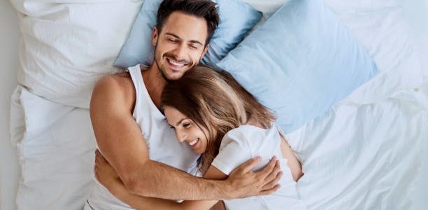 Top view of beautiful happy young couple lying on bed and hugging